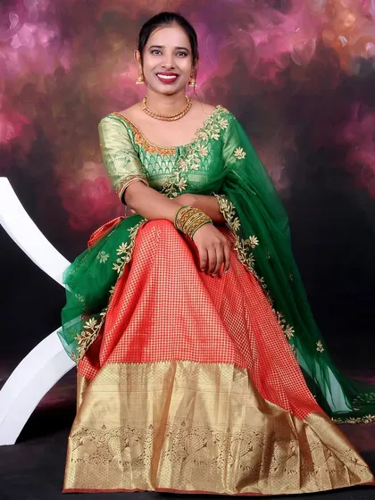 A vibrant solo portrait of a woman in beautiful traditional attire. The studio lighting makes the colors of the green and orange dress pop against the painted backdrop.
