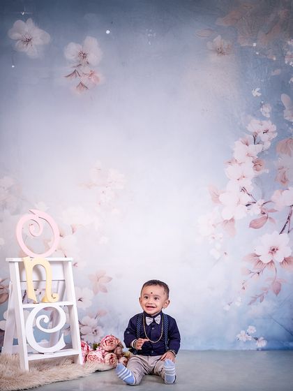 What a one-derful year it has been! This little gentleman, dressed in a bow tie and suspenders, smiles happily in a soft, floral-themed first birthday setting.