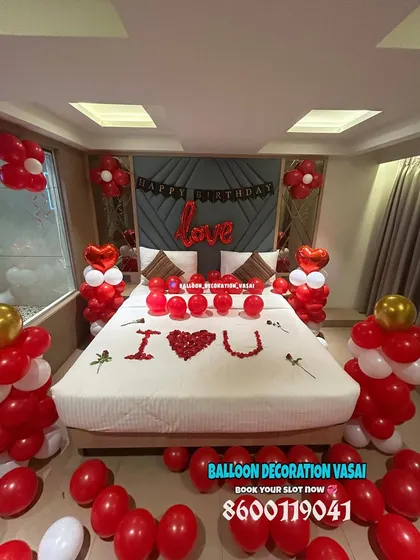 Surprise your partner with a classic romantic room decoration. This setup includes red and white balloon pillars, heart-shaped foil balloons, and a bed covered in rose petals spelling out "I ❤️ U" for a truly memorable birthday or anniversary celebration.