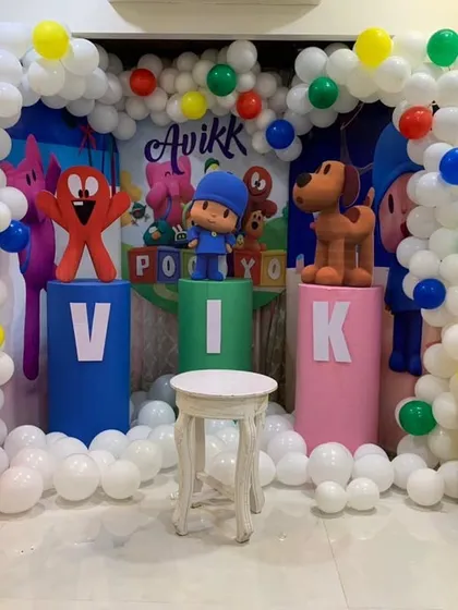 A 'Pocoyo' themed birthday setup for a home party. The decor includes character cutouts on pedestals, a themed backdrop, and a balloon arch in the show's signature colors.