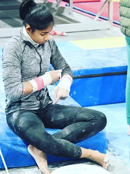 A gymnast tapes her wrists, a common practice to protect against the rigors of training on the bars.