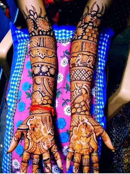 A beautiful example of a story mehendi with portraits. The design includes the couple on the palms, with peacocks, elephants, and floral bands on the arms.