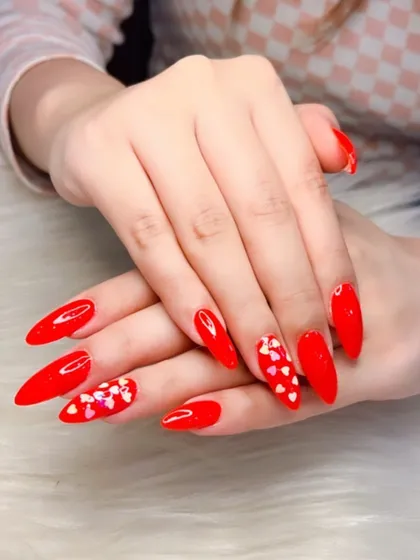 A vibrant red stiletto set perfect for Valentine's Day. The accent nails are covered in tiny, iridescent heart-shaped glitter.
