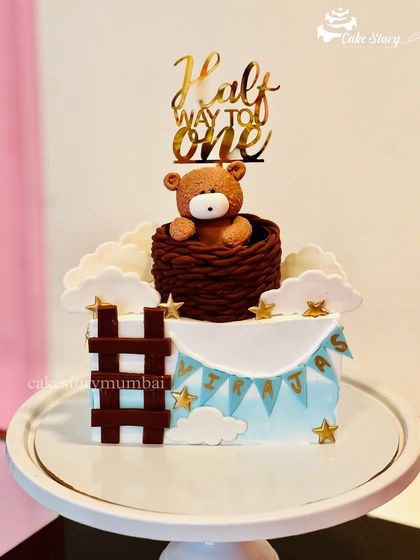 Another take on the 'Halfway to One' theme, this time with a teddy bear in a hot air balloon basket. The square cake is decorated with clouds, stars, and a mini banner.