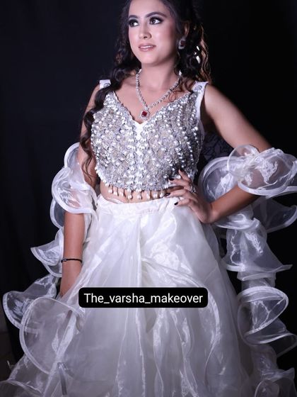 A model in a stunning white outfit with a heavily embellished pearl and crystal blouse and a ruffled organza skirt. This is a high-fashion look for a cocktail party or reception.