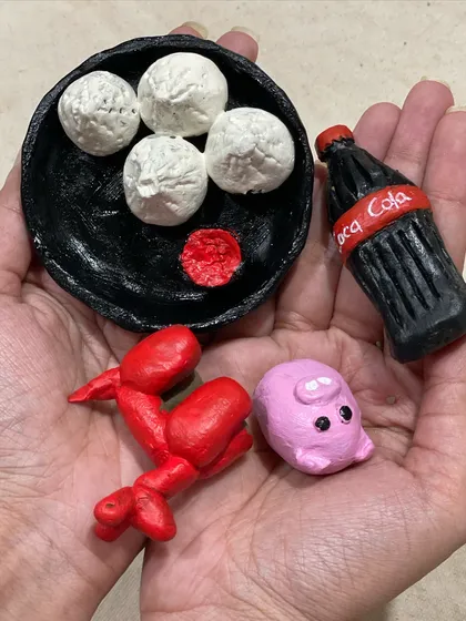 A collection of miniature clay food items, including momos and a tiny bottle of Coca-Cola. These small sculptures are so fun to make and require a delicate touch.