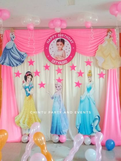 A princess themed second birthday party with pink drapes and balloon columns. The backdrop features cutouts of various Disney princesses for a royal celebration.