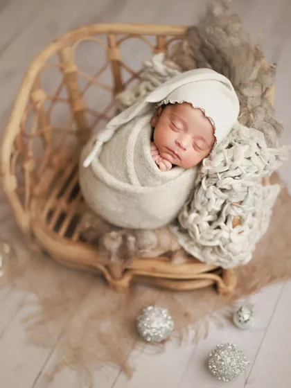 A precious moment captured in soft, neutral tones. The sleepy hat and cozy wrap in a rattan chair create a timeless and peaceful portrait.