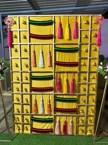 This is a unique backdrop I created for a 'Bangla' function. The golden grid frame is decorated with bells, colourful tassels, and strips of velvet cloth, creating a vibrant and traditional look perfect for home celebrations.
