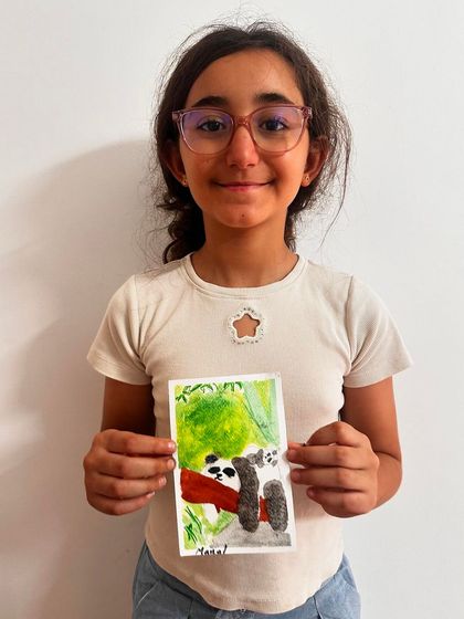 A student shows her detailed watercolor painting of a "bored panda" hanging out in a lush green tree.