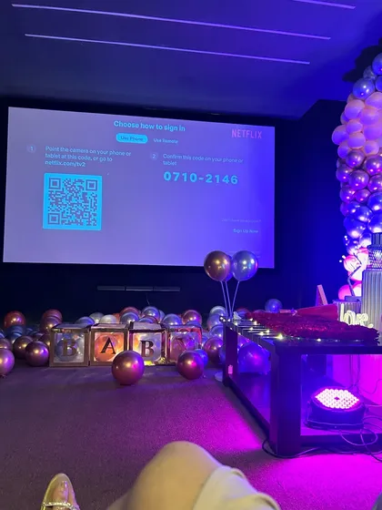 A view from the recliner, looking at the big screen ready for a Netflix session. The floor is covered in balloons and glowing "BAR" letter boxes, showing how you can personalize the space for any celebration.