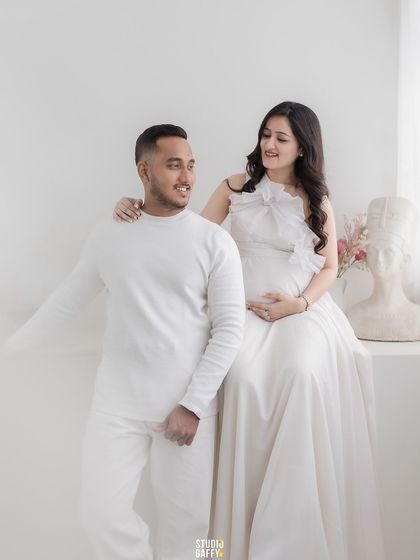 A classic couple's maternity portrait, both dressed in white, creating a clean and timeless look.