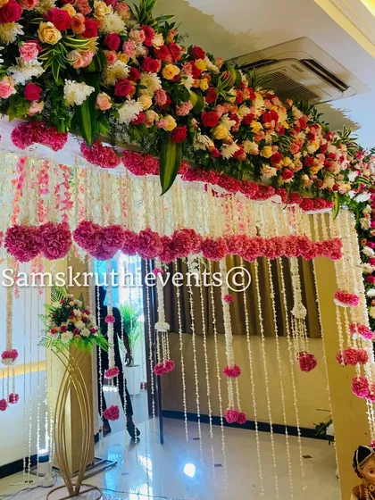 A beautiful floral entryway decoration. The arch is covered in pink and white flowers, with hanging garlands of jasmine and carnations creating a grand welcome for guests.