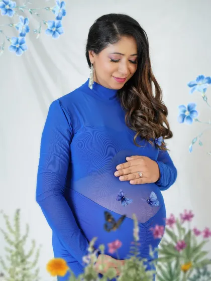 A creative and modern maternity portrait featuring a stunning royal blue gown. The artistic butterfly and floral elements add a touch of magic, highlighting the beautiful bond between mother and baby.