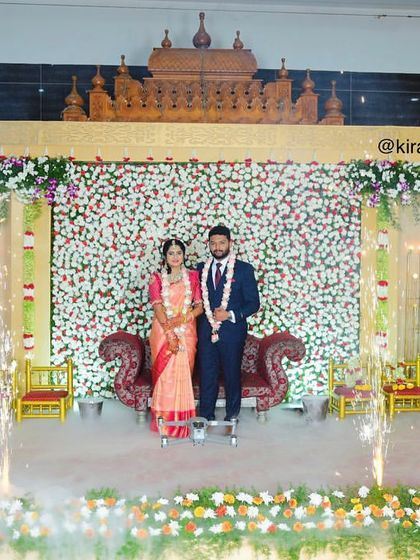 A wide shot of a reception stage featuring a flower wall, elegant seating for the couple, and cold pyro effects for a grand celebration.