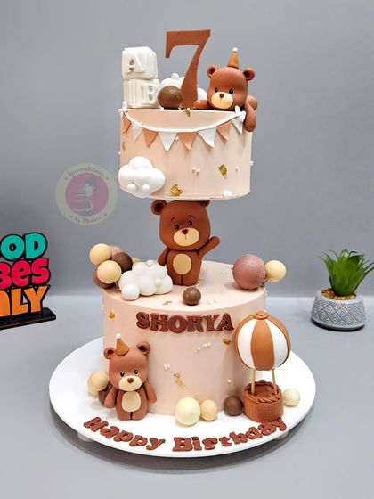 A charming anti-gravity cake featuring adorable teddy bears. The top tier floats as if held up by a strong teddy, creating a whimsical and impressive centerpiece for a birthday celebration.