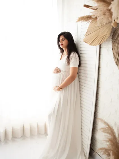 A peaceful solo portrait by the window. The mother-to-be in a simple white dress looks serene, creating a bright and airy image.