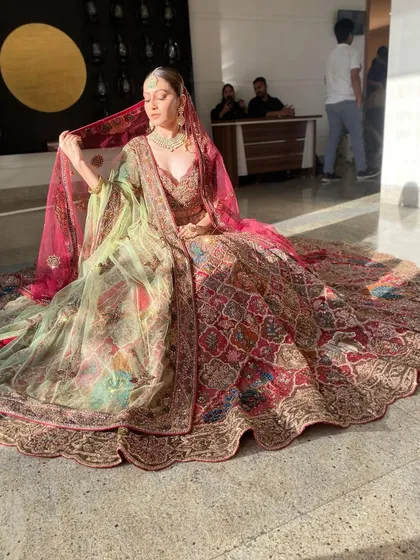 A wide shot capturing the magnificent trail of the bridal lehenga. The makeup remains a focal point, ensuring the bride's face is luminous and captivating even from a distance.