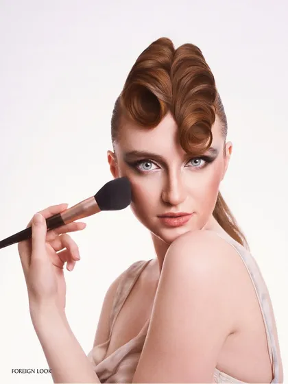 A beauty shot focused on hair and makeup. The sculpted hairstyle and sharp cat-eye makeup are the heroes, captured with clean, bright studio lighting.