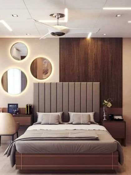 A 3D concept for a master bedroom cot. The design highlights a vertical-paneled cushioned headboard, circular backlit mirrors over the study table, and a cohesive color scheme.