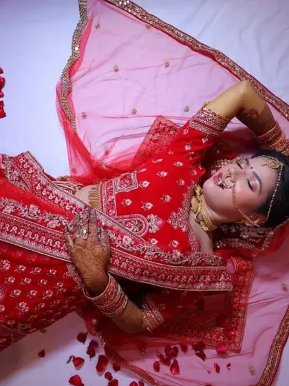 An artistic shot of the bride in her red wedding lehenga. The dramatic pose highlights the rich color of her outfit and the classic, timeless quality of her makeup.