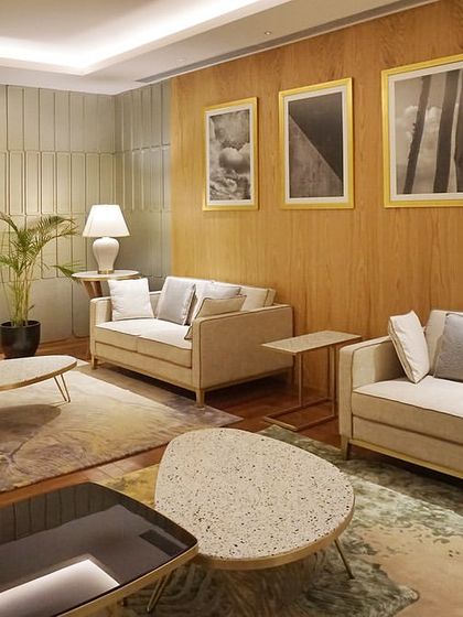 The Private Lounge at the 'Reserved Lounges' in Bangalore. The space is designed as a quiet retreat, with comfortable sofas, warm wood paneling, and curated artwork creating a calm and sophisticated ambiance.