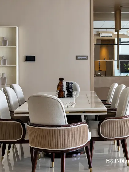A full view of a luxurious dining room, featuring plush, two-toned chairs and a sleek white table. A mirrored wall in the background adds depth and reflects light, making the space feel larger.