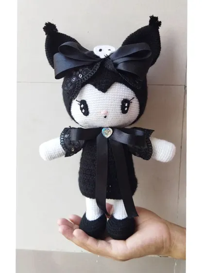 This is Kuromi from the Sanrio universe, made with black yarn and decorated with satin ribbons and a heart gem for a special touch.