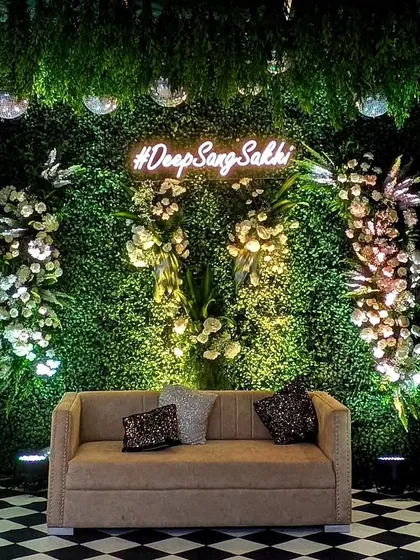 A chic photo booth for a Sangeet night, featuring a lush green wall, a custom neon hashtag, and sparkling disco balls for that perfect party vibe.