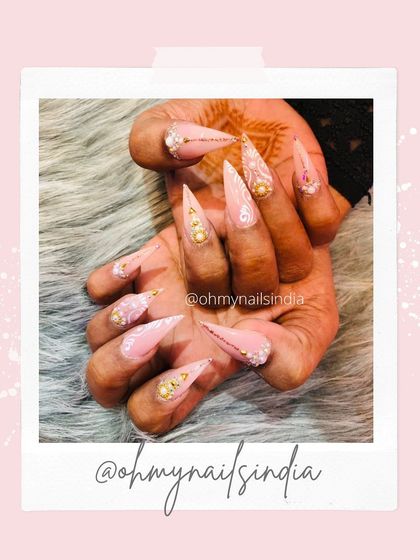 Your nails are jewels. This extravagant set features long stiletto nails adorned with a mix of gold studs, pearls, and delicate floral details for a truly opulent look.