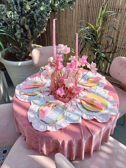 A beautiful overhead view of a table setting, showcasing the layers of detail. A pink velvet tablecloth is topped with patterned placemats, bright yellow plates, and a delicate centerpiece of pink flowers and candles.
