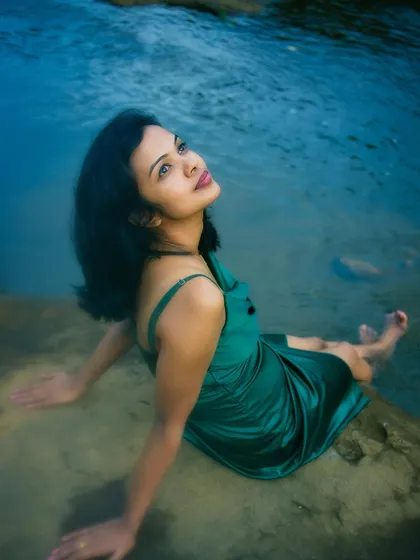 A vibrant portrait of a woman in a green dress sitting at the edge of a body of water, looking up towards the sky. The rich blues and greens highlight my work with natural light and vivid color.