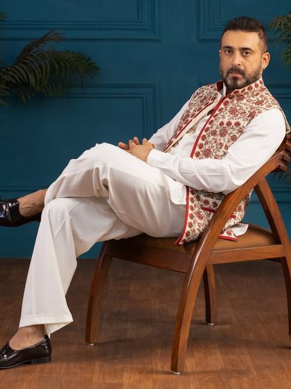 Explore my collection of Kashmiri art work. Here I am seated, wearing an off-white kurta and salwar paired with a vibrant embroidered jacket.