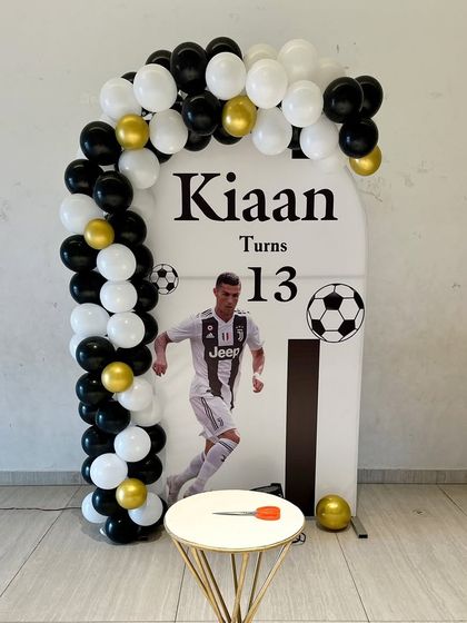 A football-themed setup for a 13th birthday. The decor features a personalized backdrop with the birthday boy's favorite player, a simple balloon arch, and a soccer ball motif.