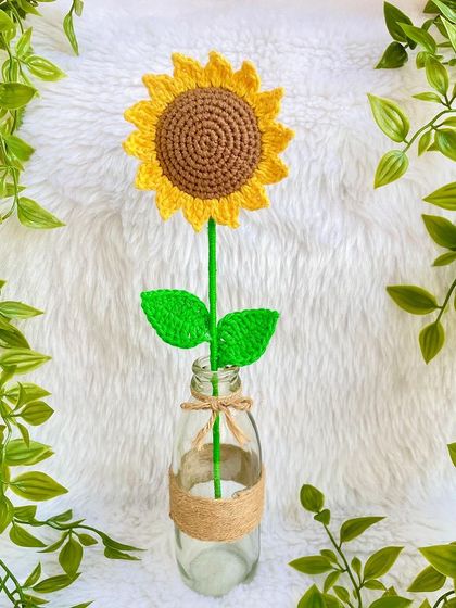 A single crochet sunflower placed in a rustic glass bottle vase. It shows how beautifully these stems can be displayed as home decor.
