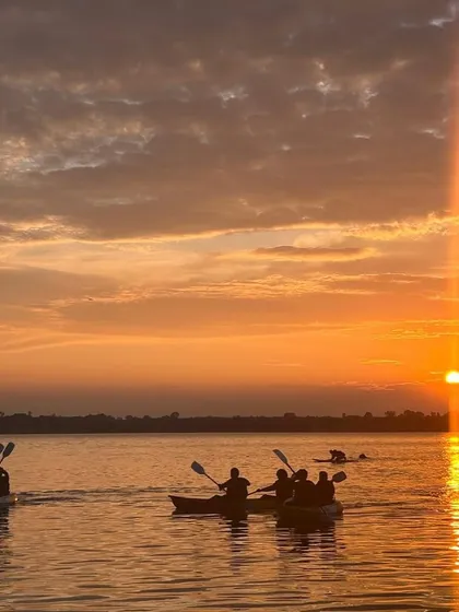 A group of kayakers paddles together as the sun sets, casting a warm orange glow over the water.