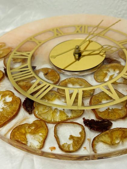 A close-up of the fruit slice clock, showing the details of the preserved orange and strawberry pieces. The gold Roman numeral clock face adds a touch of elegance to the rustic design.