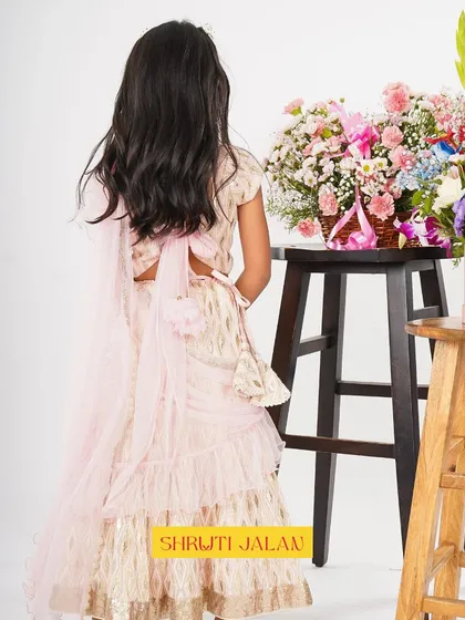 A back view of the cream and gold printed lehenga, showing the delicate bow and the soft, ruffled dupatta.