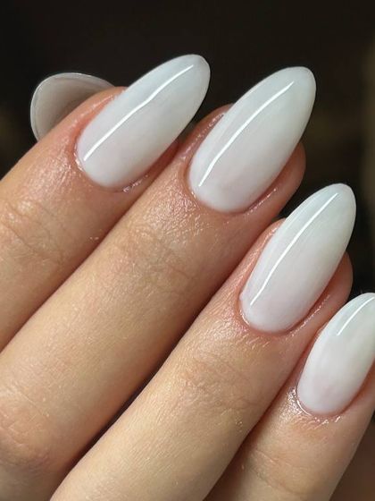 A clean, opaque white manicure on long, almond-shaped nails. The bright white and elegant shape create a striking and modern look.
