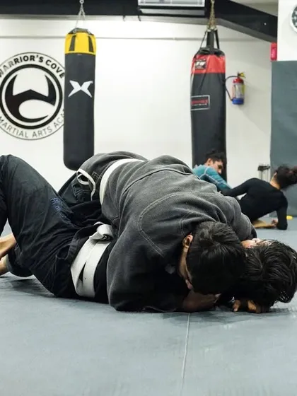 Two students in traditional white and black Gis work on passing the guard. The Gi adds a layer of complexity, teaching you to use grips to your advantage.