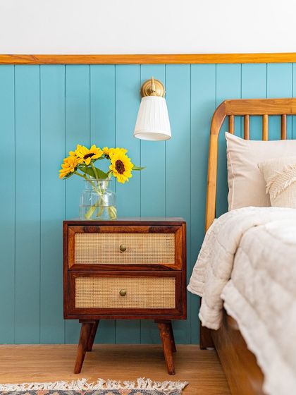 In this master bedroom, a light blue paneled wall evokes the serenity of a clear sky. I styled the wooden and cane side table with bright sunflowers to bring a touch of nature and cheer indoors.