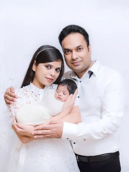 A classic first family portrait with a newborn. The parents look proudly at the camera, holding their new baby, marking the beginning of their journey.