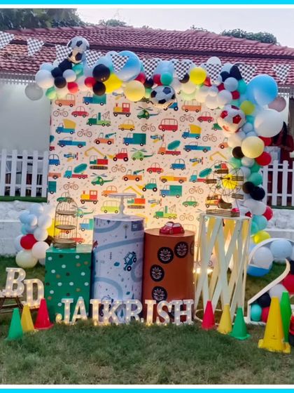 An outdoor Cars-themed second birthday party. The setup includes a traffic-themed backdrop, a mini ride-on car, and traffic cone props.