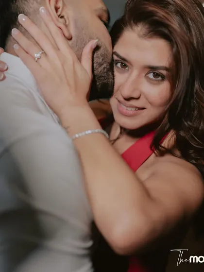 An intimate and alluring portrait. The groom whispers to the bride as she looks directly at the camera, her hand gently on his face, showcasing her engagement ring.