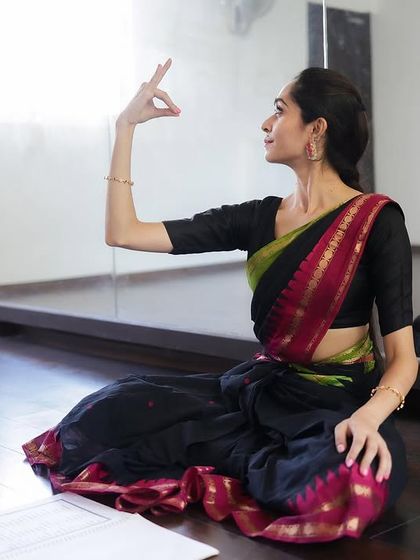 Demonstrating a mudra while seated, with my notes nearby. I combine traditional teaching with structured lesson plans to provide a comprehensive learning experience.