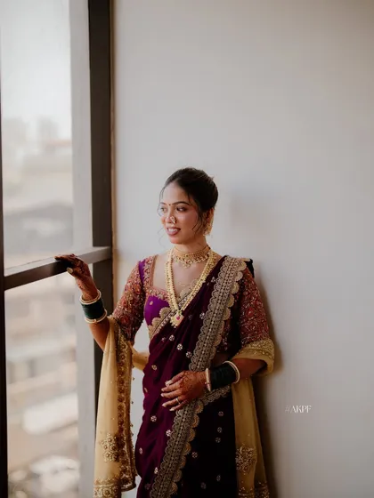 A candid shot of a bride in her purple Nauvari saree. The makeup is kept natural and elegant to let her happiness shine through, complemented by a simple bun and gold jewellery.