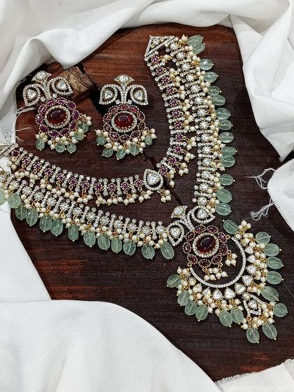 A layered necklace set with a long Rani Haar and a matching choker. This design is perfect for brides, featuring rich green or red stones and intricate detailing for a complete and opulent look.