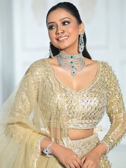 A smiling model wearing our gold sequin lehenga. The outfit pairs beautifully with diamond jewelry for a chic and polished look.