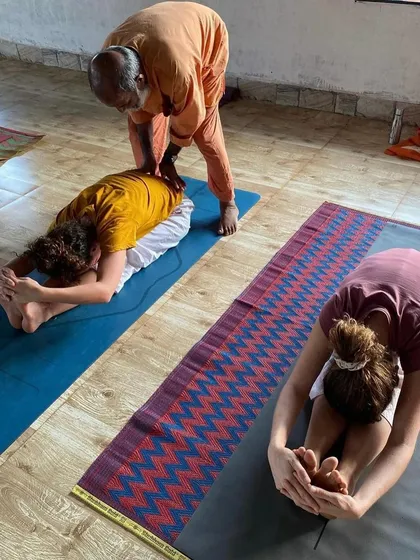In our Hatha yoga sessions, I provide personal guidance to ensure proper alignment and understanding of each asana. Here, I am assisting a student in Paschimottanasana, the seated forward bend, to help them safely deepen the posture.