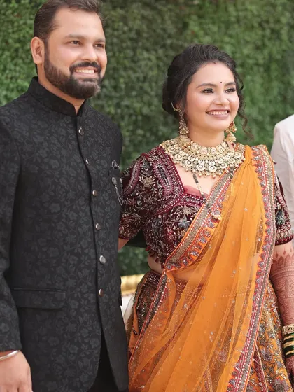 A happy couple portrait. The bride's orange lehenga and the groom's classic black sherwani create a beautiful and elegant contrast.